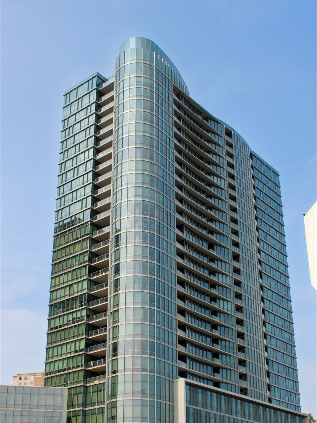 Curved glass curtain wall high-rise tower with tiered balconies against a clear blue sky